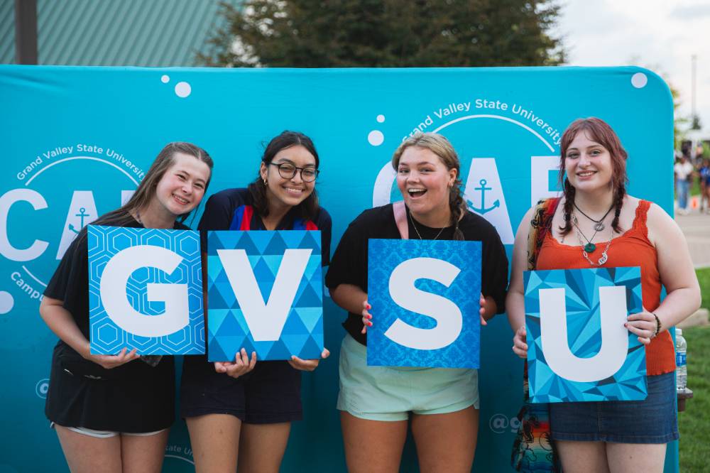 four students holding GVSU letters, smiling and posing in front of CAB backdrop at Laker Kickoff photo booth